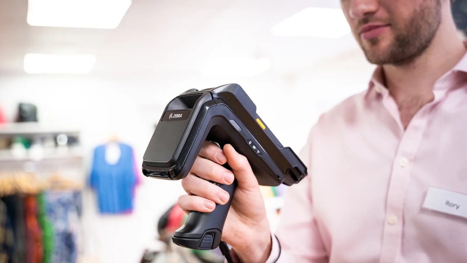 Shop assistant holding a Zebra RFD40 sled with a Zebra TC22 handheld fitted, in a clothing shop